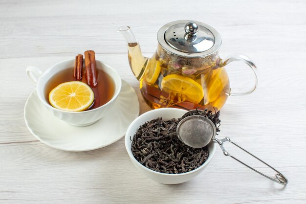 Vue latérale de l'heure du thé avec une tisane mélangée au citron dans une tasse et un pot sur un tableau blanc