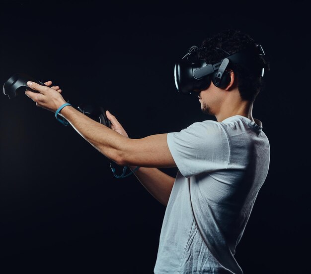 Vue latérale d'un homme aux poils vêtu d'une chemise blanche jouant à des jeux avec des lunettes de réalité virtuelle. Isolé sur fond sombre.