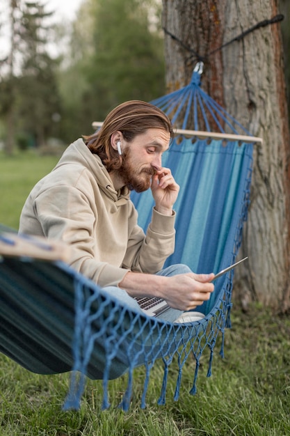 Vue latérale de l'homme dans un hamac avec ordinateur portable