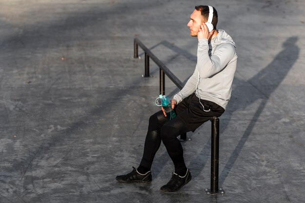 Vue latérale homme écoutant de la musique et tenant une bouteille d'eau