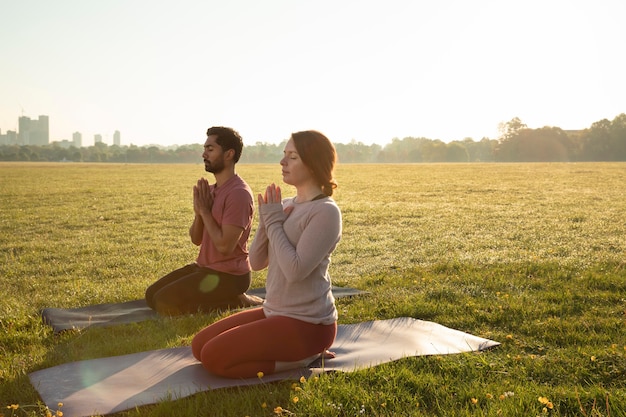 Photo gratuite vue latérale d'un homme et d'une femme méditant à l'extérieur sur des tapis de yoga