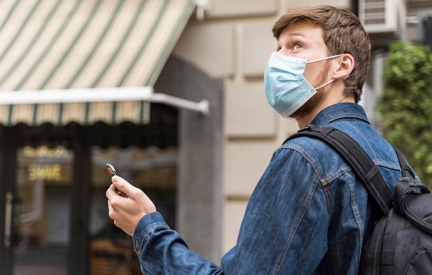 Vue latérale homme marchant à l'extérieur avec un masque médical sur