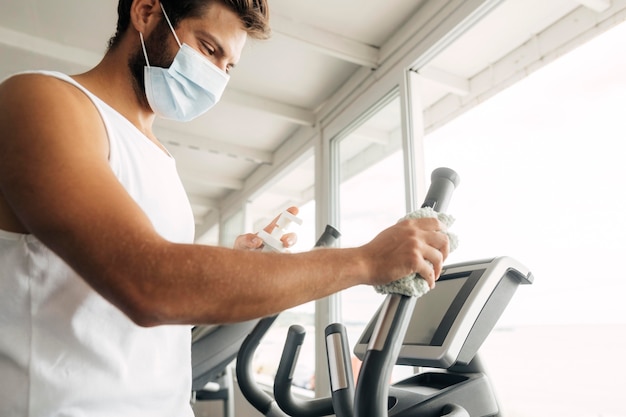 Vue latérale de l'homme avec un masque médical à l'aide d'équipement de gym