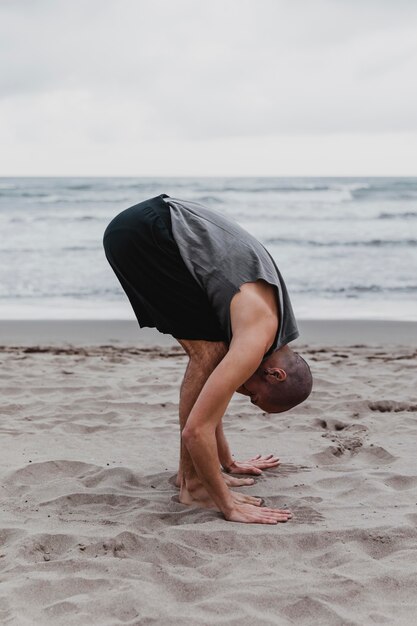 Vue latérale de l'homme sur la plage, exerçant des positions de yoga