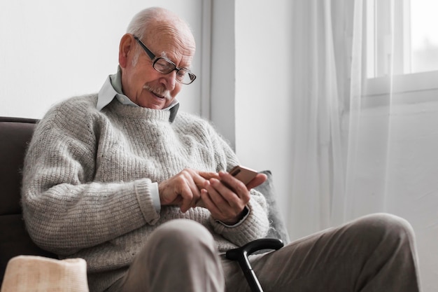 Vue latérale d'un homme plus âgé dans une maison de soins infirmiers à l'aide de smartphone