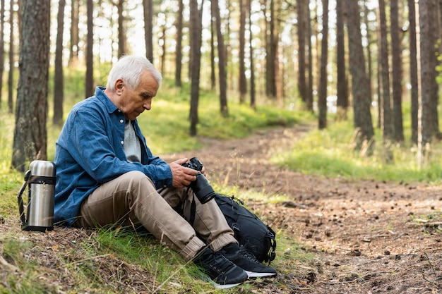 Vue latérale d'un homme plus âgé tenant la caméra tout en se reposant dans la nature