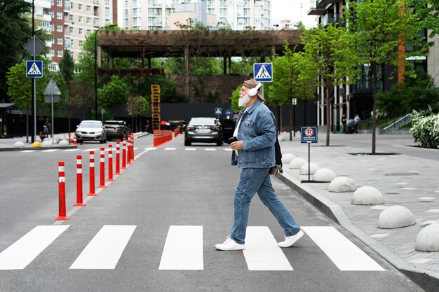 Vue latérale d'un homme plus âgé traversant la rue tout en écoutant de la musique au casque