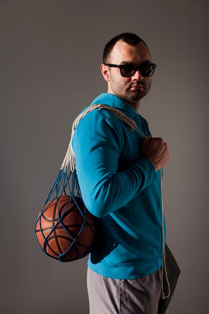 Vue latérale d'un homme portant des lunettes de soleil tenant un ballon de basket en filet sur l'épaule