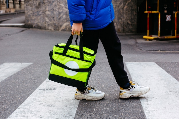 Vue latérale l'homme porte l'ordre dans un sac vert clair sur la route piétonne zèbre