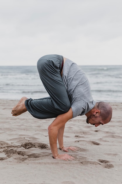 Vue latérale de l'homme pratiquant des positions de yoga sur la plage