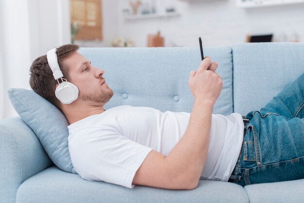 Vue latérale homme restant sur le canapé et regardant sur son téléphone