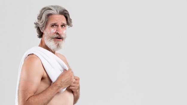 Vue latérale d'un homme senior avec une serviette après la douche et une crème hydratante