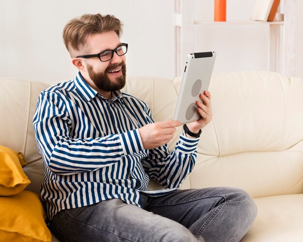 Vue latérale de l'homme souriant sur canapé avec tablette