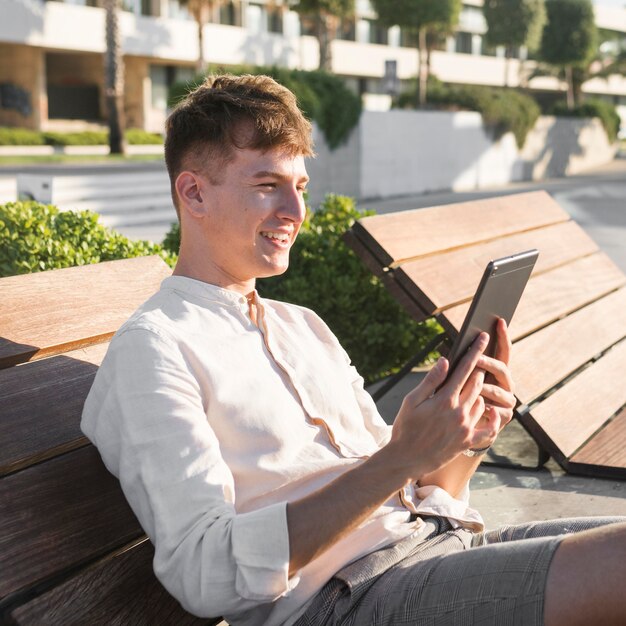 Vue latérale de l'homme souriant regardant la tablette à l'extérieur