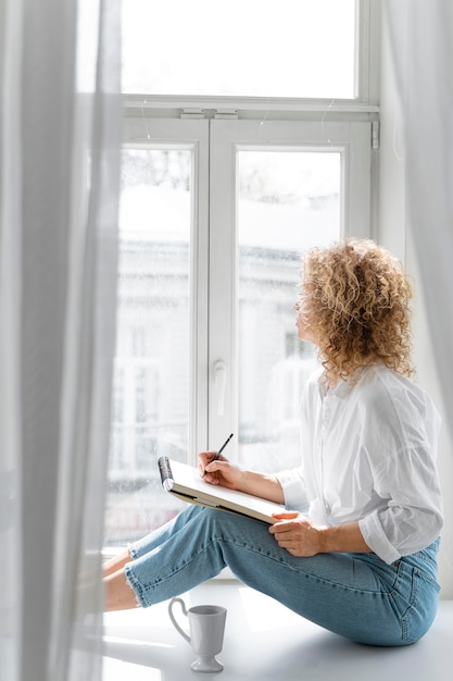 Photo gratuite vue latérale d'une jeune femme dessin à la maison près de la fenêtre