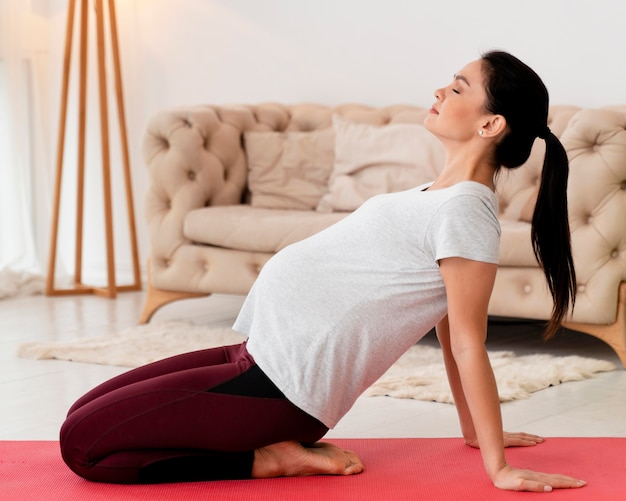 Vue latérale jeune femme enceinte exerçant sur tapis de fitness