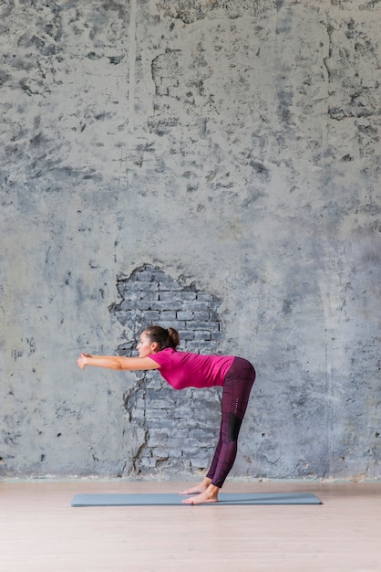 Vue latérale d&#39;une jeune femme faisant des exercices d&#39;étirement sur fond gris