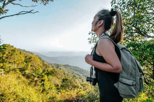 Vue latérale Jeune femme de randonnée asiatique debout au point de vue et regardant belle vue avec heureux sur la montagne de pointe et l'espace de copie de rayon de soleil