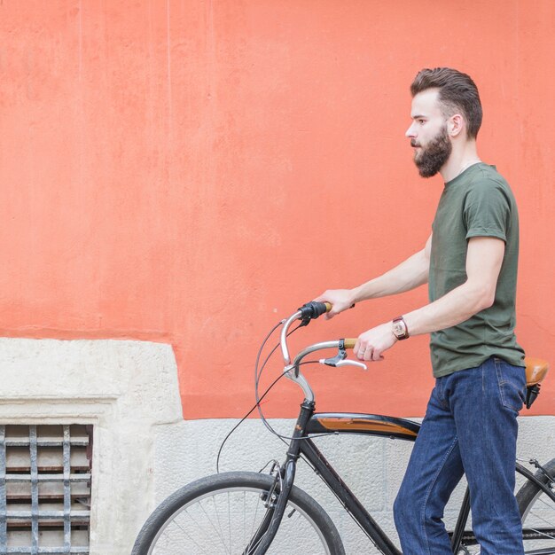 Vue latérale d&#39;un jeune homme debout avec sa bicyclette