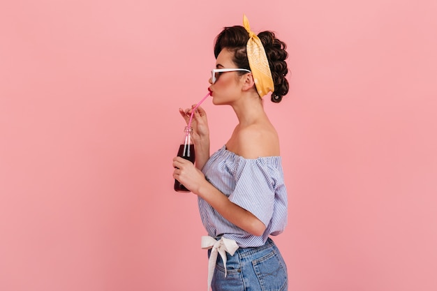 Vue latérale d'une jolie pin-up aux cheveux noirs. Photo de Studio de jolie fille en tenue rétro, boire des boissons.