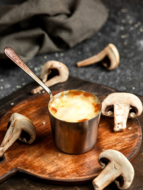 Vue latérale de la julienne de champignons cuits au four avec du poulet et du fromage dans un petit bol sur planche de bois