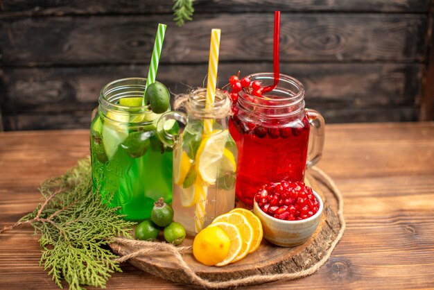 Vue latérale de jus de fruits frais biologiques en bouteilles servis avec des tubes et des fruits sur une planche à découper en bois