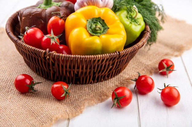 Vue latérale des légumes comme l'aneth poivron ail tomate dans le panier et sur un sac sur bois