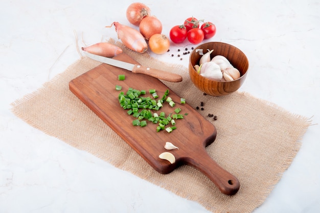 Vue latérale des légumes comme l'oignon vert sur une planche à découper tomate à l'ail avec un couteau sur fond blanc avec copie espace