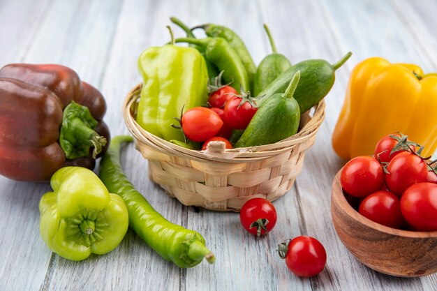 Vue latérale des légumes comme tomate concombre poivron dans un bol panier et sur bois