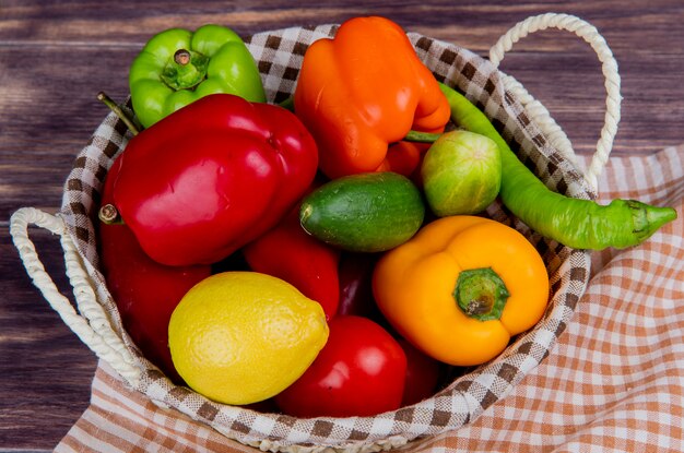 Vue latérale des légumes comme tomate poivron concombre dans le panier sur tissu à carreaux et table en bois