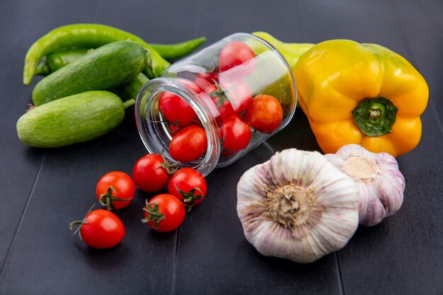 Vue latérale des légumes comme des tomates débordant de concombre ail et poivron sur fond noir