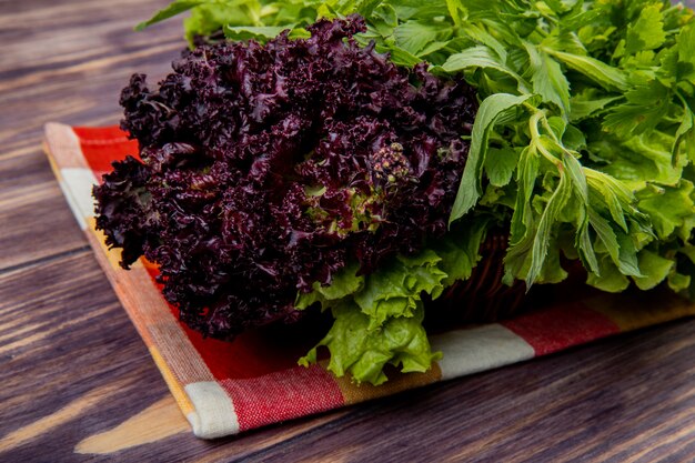 Vue latérale de légumes verts comme la laitue menthe coriandre basilic dans le panier sur le tissu sur la table en bois