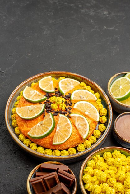 Vue latérale de loin gâteau et bonbons gâteau avec tranches de citron vert et bols de chocolat citrons jaunes bonbons chocolat et crème au chocolat sur la table