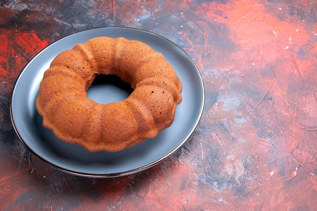 Vue latérale de loin un gâteau rond appétissant sur l'assiette sur la table sombre