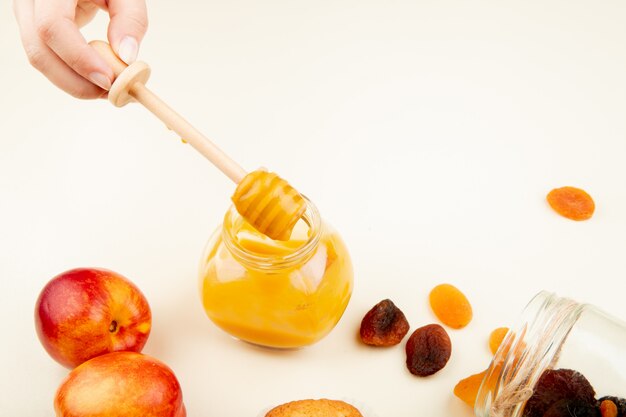 Vue latérale de la main de la femme tenant un bocal en verre de confiture de pêches aux raisins secs sur blanc