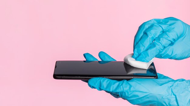 Vue latérale des mains avec des gants chirurgicaux désinfectant le smartphone