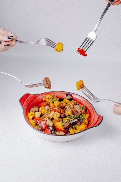 Vue latérale des mains tenir les fourchettes sur le bol avec des pommes de terre et des légumes à base de viande cuite