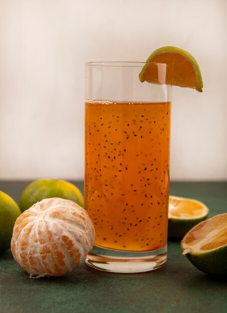 Vue latérale des mandarines saines et fraîches avec du jus de fruits frais dans un verre sur un mur blanc