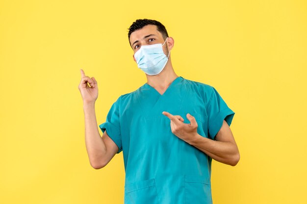 La vue latérale d'un médecin dans le masque dans l'uniforme médical pointe vers le côté