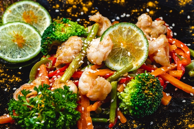 Vue latérale mélanger les légumes crevettes grillées avec brocoli carotte poivron haricots verts tranches de citron vert et graines de sésame sur une plaque