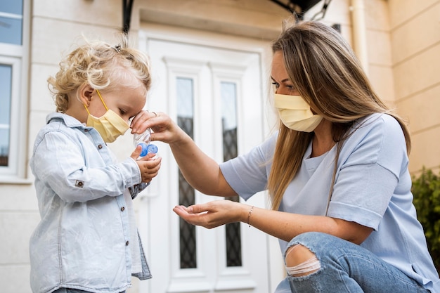 Vue latérale de la mère et de l'enfant avec des masques médicaux et un désinfectant pour les mains