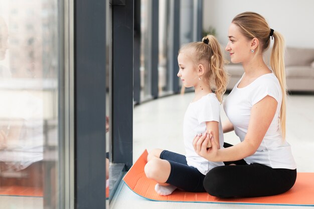 Vue latérale de la mère faisant du yoga avec sa fille à la maison