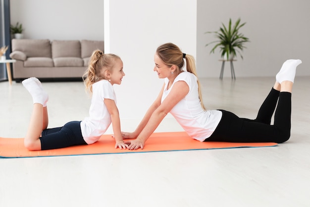 Photo gratuite vue latérale de la mère et la fille exerçant sur un tapis de yoga à la maison