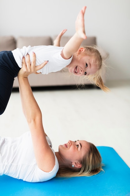 Vue Latérale De La Mère Sur Un Tapis De Yoga Soulevant Une Fille Heureuse