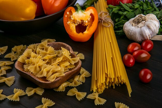 Vue latérale des moitiés de poivrons multicolores avec des spaghettis crus et pâtes ail et tomates sur une surface en bois