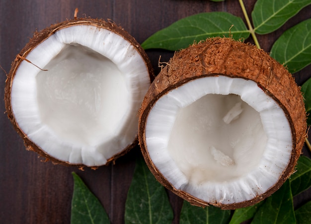 Vue latérale des noix de coco fraîches et brunes avec des feuilles sur la surface en bois