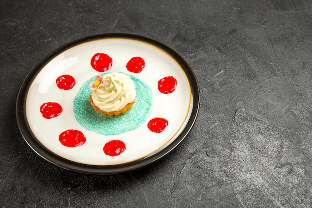 Vue latérale de la nourriture savoureuse sur la plaque blanche un cupcake appétissant avec des sauces sur la surface sombre