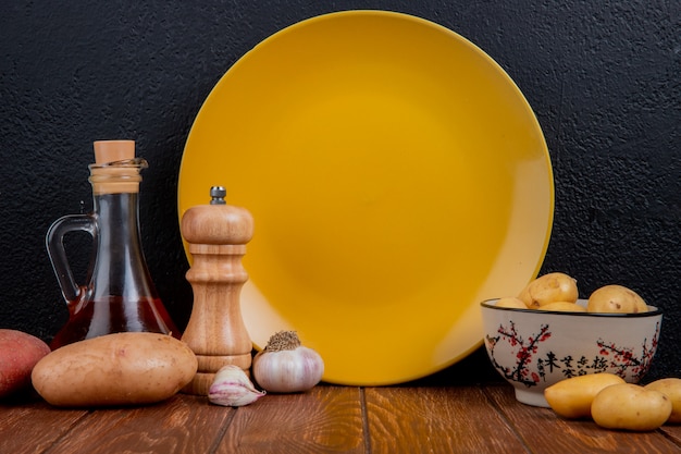 Vue latérale de nouvelles pommes de terre dans un bol avec du rouge et du blanc, du sel d'ail au beurre fondu et une assiette vide sur une surface en bois et une surface noire