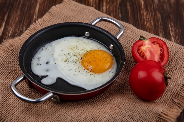 Vue latérale oeuf au plat dans une casserole avec des tomates sur une serviette beige sur un fond en bois