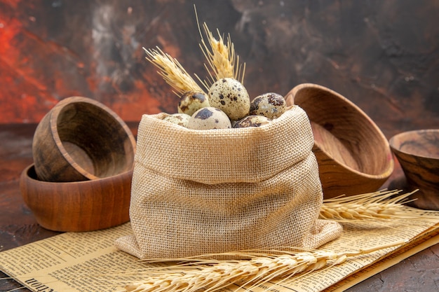 Photo gratuite vue latérale des œufs frais de la ferme dans un sac en tissu blanc et des pots en bois sur un vieux journal sur fond marron